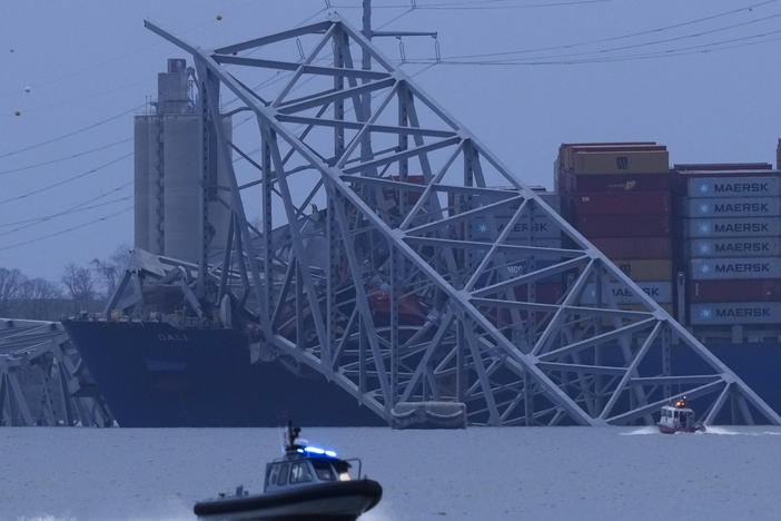 A container ship rests against wreckage of the Francis Scott Key Bridge as night falls on Tuesday, as seen from Sparrows Point, Md.