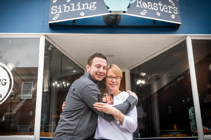 Sibling Coffee Roasters owner Libby Powell poses with her brother, Benjamin Withem, outside her West Virginia coffee shop. In her hand is an early photo of the pair — one they are trying to re-create.