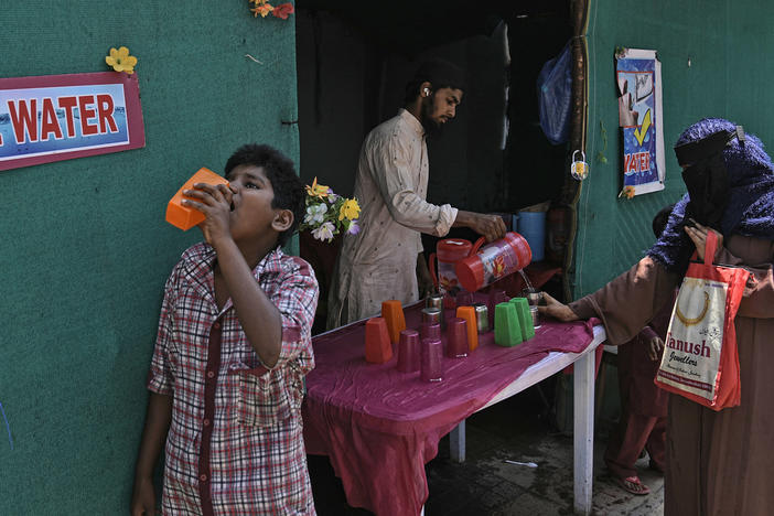 A volunteer distributes drinking water next to a bus stand on a hot summer day in Hyderabad, India, Thursday, March 21, 2024.