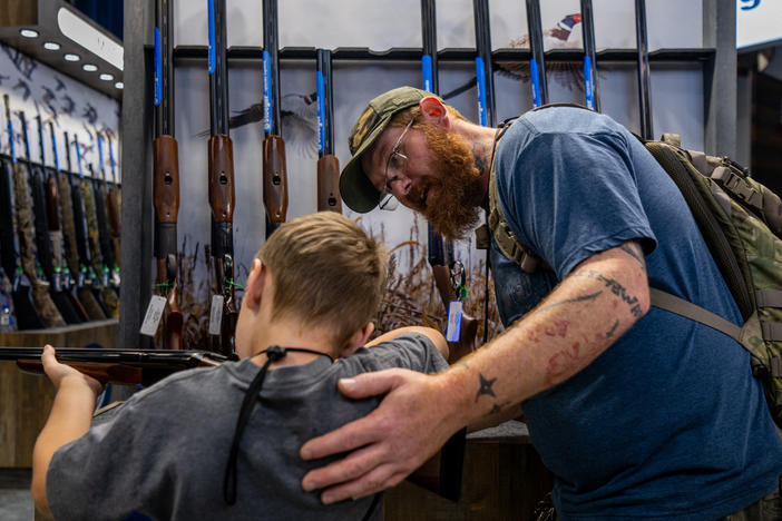 A father helps his son steady a firearm at the National Rifle Association (NRA) annual convention on May 28, 2022, in Houston, Texas. Exposing children to guns comes with risks, but some firearms enthusiasts say they'd prefer to train kids to use guns responsibly.