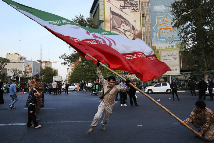 Demonstrators wave a huge Iranian flag in their anti-Israeli gathering in front of an anti-Israeli banner on the wall of a building at the Felestin (Palestine) Sq. in Tehran, Iran, Monday, April 15, 2024.