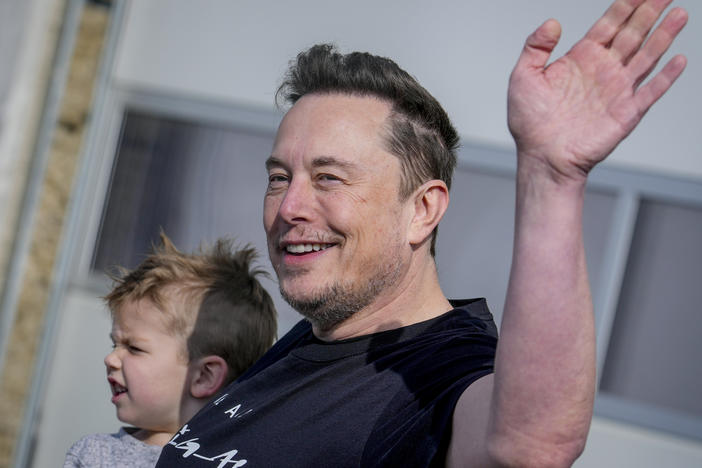 With his son in one arm, Tesla CEO Elon Musk waves while visiting the Tesla Gigafactory in Germany in March.