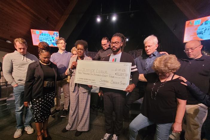 Members of the Sycamore Creek Church congregation bow their heads and pray over Justice League of Greater Lansing leaders, Willye Bryan and Prince Solace, as they hold a large check.