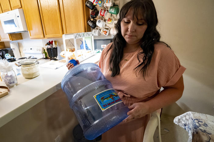Richelle Dietz holds an empty five-gallon water bottle at her home in Joint Base Pearl Harbor-Hickam, Monday, April 22, 2024, in Honolulu, Hawaii. The Dietz family relies on bi-weekly water deliveries for basic needs since their water was tainted in 2021.