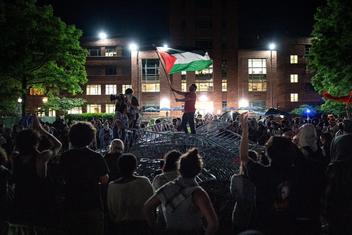 A man holds up a Palestinian flag as activists and students surround piled barricades at an encampment at at George Washington University early Monday.