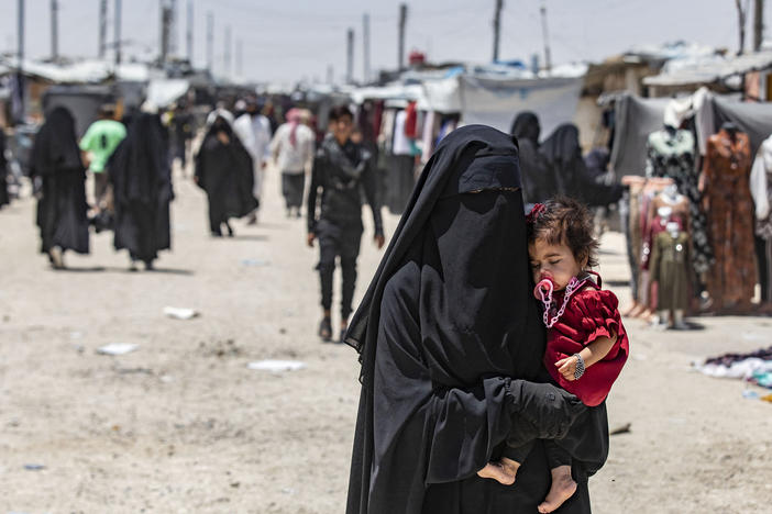 A woman carries a child as she walks through the al-Hol refugee camp in northeastern Syria in Oct. 2023.