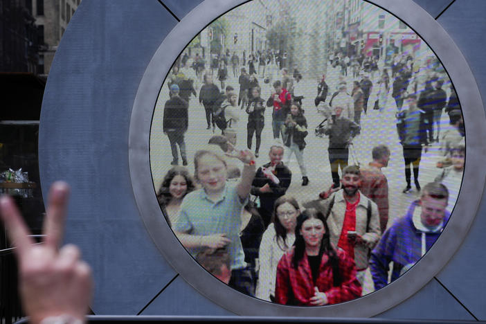 People in both New York and Dublin, Ireland, wave and signal at each other while looking at a livestream view of one another as part of an art installation on the street in New York, Tuesday, May 14, 2024.