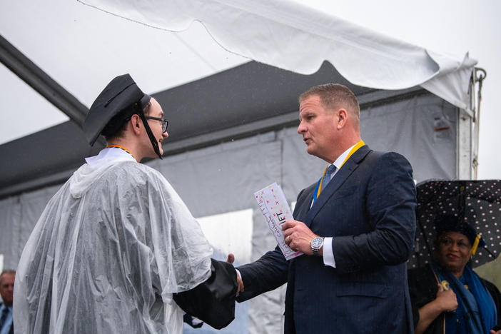 Robert Hale gives an envelope with cash to a graduating UMass Dartmouth student at last week's commencement. Each of the 1,200 graduates received $1,000 onstage, half to keep and half to donate.