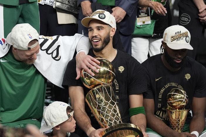 Boston Celtics forward Jayson Tatum, center, holds the Larry O'Brien Championship Trophy as he celebrates with center Kristaps Porzingis, left, and guard Jaylen Brown, right, after the Celtics won the NBA championship with a Game 5 victory over the Dallas Mavericks on Monday in Boston.