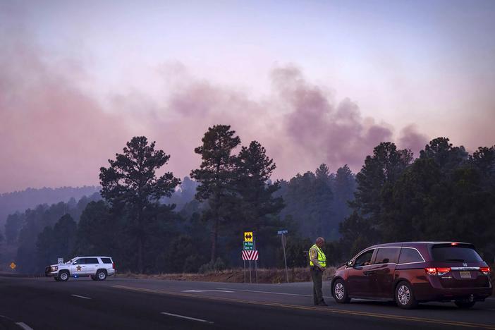 Smoke from the South Fork Fire reflects a pink hue during sunrise Tuesday as law enforcement officers turn drivers away on State Road 48 at State 220 because of wildfires burning near Ruidoso, N.M. 