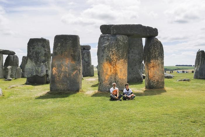 In this handout photo, Just Stop Oil protesters sit after spraying an orange substance on Stonehenge, in Salisbury, England, on Wednesday. (Just Stop Oil via AP)