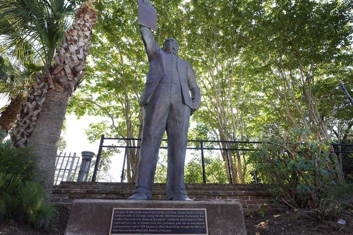 In this June 17, 2020, photo, a statue depicts a man holding the state law that made Juneteenth a state holiday in Galveston, Texas. 