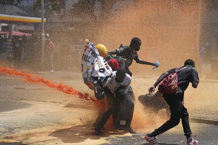 Protesters scatter as Kenyan police spray water canon at them during a protest over proposed tax hikes in a finance bill in downtown Nairobi, Kenya, on Tuesday.