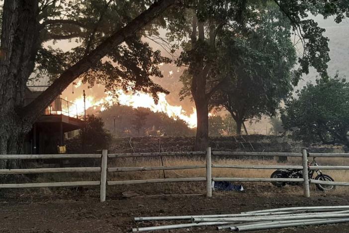 In this photo provided by Alison Oszman, a fast-moving wildfire near the Oregon-Idaho border moves toward a home on Rye Valley Lane in Huntington, Ore., on Wednesday afternoon.