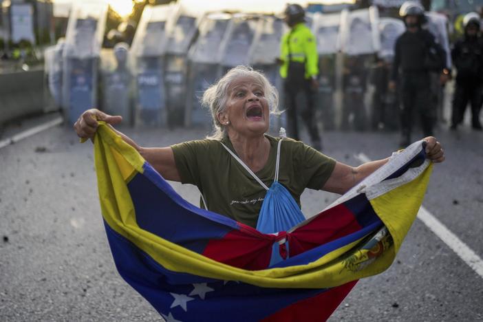 Consuelo Marquez holds a Venezuelan flag in front of police blocking demonstrations against the official election results declaring President Nicolás Maduro's reelection, the day after the vote in Caracas, Venezuela, Monday.