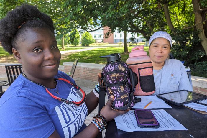 Admire Stewart and Margie Rodriguez hold up water bottles that Rodriguez purchased for housekeepers at the University of Maryland. Hydration is a challenge when the housekeepers work long hours in unairconditioned dormitories across campus.