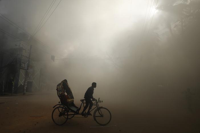 A rickshaw puller rides in the smoke caused by a burning shopping center that was set on fire by protesters during a rally against Prime Minister Sheikh Hasina and her government in Dhaka, Bangladesh, on Sunday.