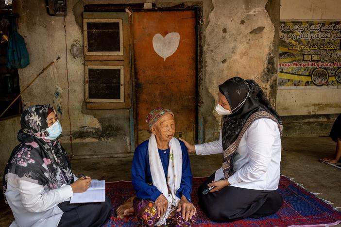 Two health workers see a patient.  “Cataract cut my main income source," the patient said before she had surgery. "I cannot sell anything, I cannot write anything. It’s difficult to continue with my job.”  