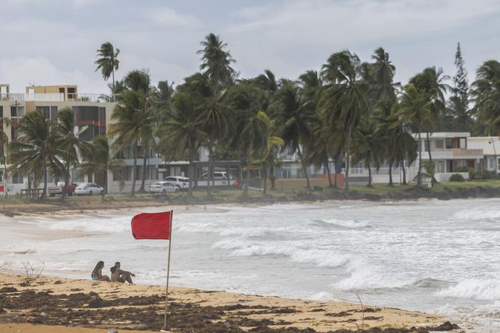 Tourists sit on La Pared beach as Ernesto passes by Luquillo, Puerto Rico, on Tuesday.