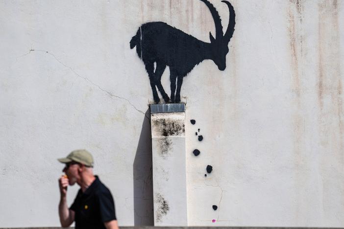 A man eats an apple as he walks past a mural depicting a goat, purportedly by the street artist Banksy, on August 5, 2024 in the Richmond borough of London, England. 