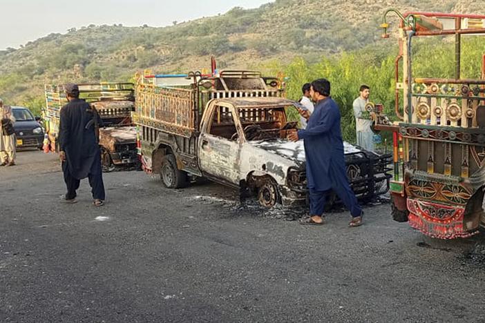 People near burned vehicles, torched by gunmen after killing passengers, on a highway in Musakhail, a district in Baluchistan province in southwestern Pakistan on Monday.