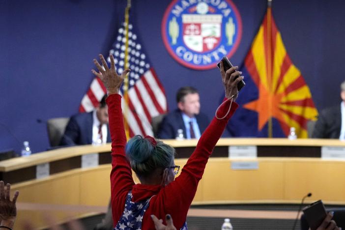 A woman stands in protest as the Maricopa County Board of Supervisors meets to discuss general election results on Nov. 28, 2022, in Phoenix.