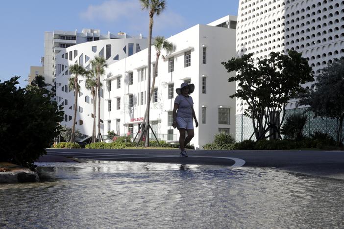 A woman walks along a flooded street caused by a king tide in Miami Beach, Fla., in 2019. So-called sunny day floods are getting more common in many coastal areas as seas rise due to human-caused climate change.