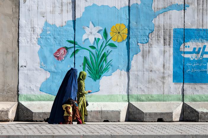 An Afghan burqa-clad woman walks past a wall mural with the map of Afghanistan, in Kabul on February 1, 2024. 
