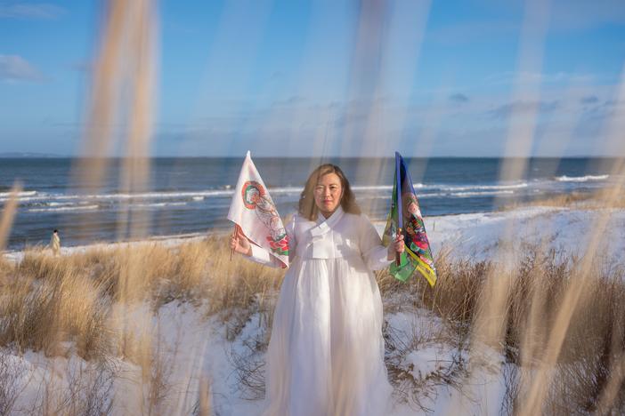 <em>Helena Soholm holds up the five directional flags of Korean shamanism in Dronningmølle, Denmark.</em>