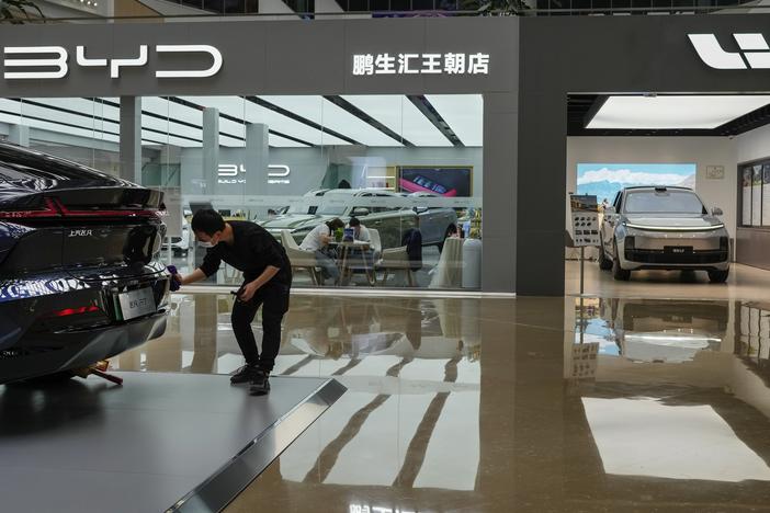 A worker wipes a Rising F7 car model at a floor section selling various Chinese-made electric car brands inside a shopping mall in Beijing, Tuesday, April 4, 2023. (AP Photo/Andy Wong)