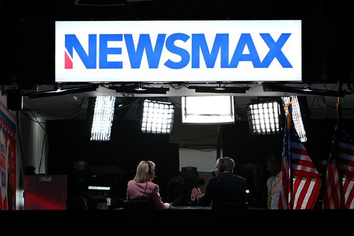 News anchors work at Newsmax's booth during the 2024 Republican National Convention in Milwaukee, Wisconsin. The network has settled with voting-tech company Smartmatic, which accused it of defamation following the 2020 presidential election. 