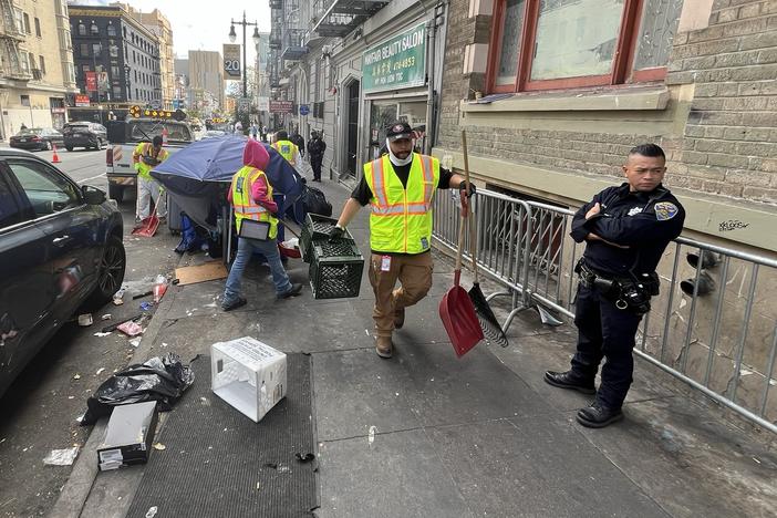 San Francisco police officers keep an eye on city workers as they sweep unsanctioned tents and belongings from a street in the Tenderloin.
