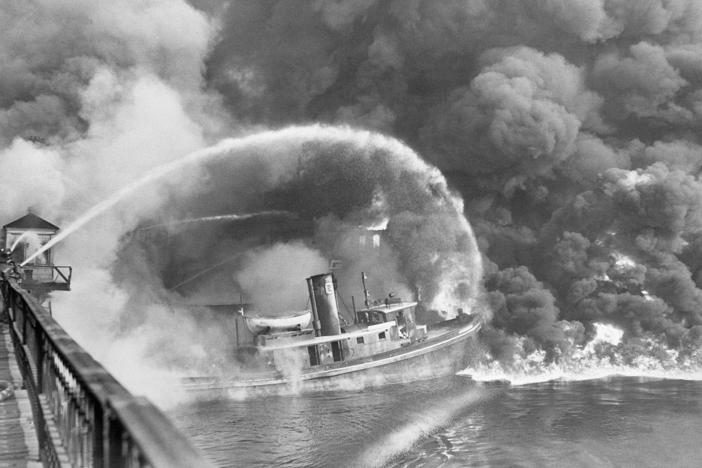 Firefighters stand on a bridge over the Cuyahoga River to spray water on the tug Arizona as a fire, started in an oil slick on the river, engulfs docks in Cleveland on Nov. 1, 1952.
