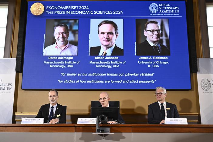 Academy of Sciences permanent secretary Hans Ellegren (C), Jakob Svensson (L) and Jan Teorell of the Nobel Assembly sit in front of a screen displaying the laureates (L-R) Turkish-American Daron Acemoglu and British-Americans Simon Johnson and James Robinson of the 2024 Sveriges Riksbank Prize in Economic Sciences in Memory of Alfred Nobel during the announcement by the Royal Swedish Academy of Sciences in Stockholm, Sweden on October 14, 2024. (Photo by Christine Olsson/TT / TT NEWS AGENCY / AFP) / Sweden…