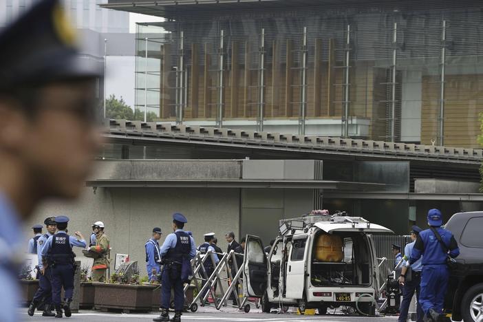 Police officers work near a vehicle, center, which was stuck against a barricade near the prime minister's office, background, in Tokyo on Saturday.