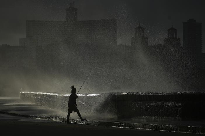 A person fishes along the boardwalk as waves crash during a power outage in Havana, Monday, Oct. 21, 2024.