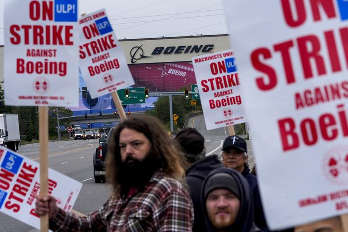 Boeing workers wave picket signs to passing drivers as they strike in Everett, Wash.. The machinists walked off the job more than six weeks ago as they bargain for higher pay and a return of their pension plan.