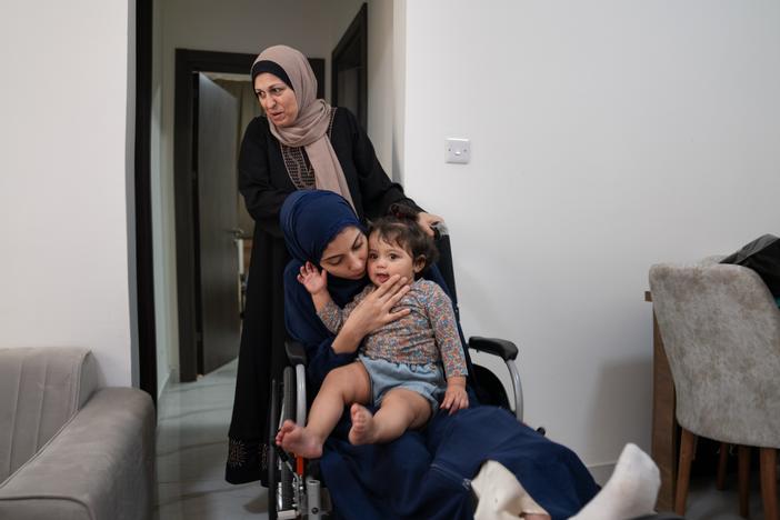 Raneem Hijazi holds her baby, Mariam, on her lap in her wheelchair, as Hijazi's mother-in-law, Soha Sakallah (standing), helps her.