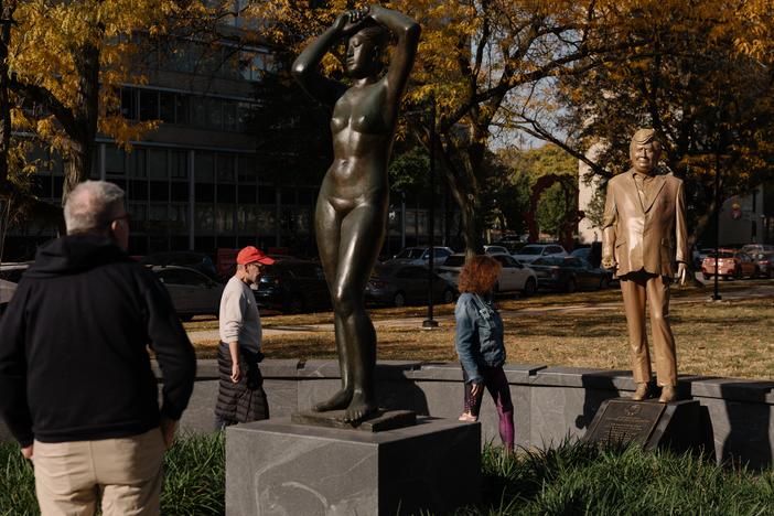 Pedestrians look at a statue of Donald Trump behind Gerhard Marcks' sculpture <em>Maja</em>, in Maja Park in Philidelphia.