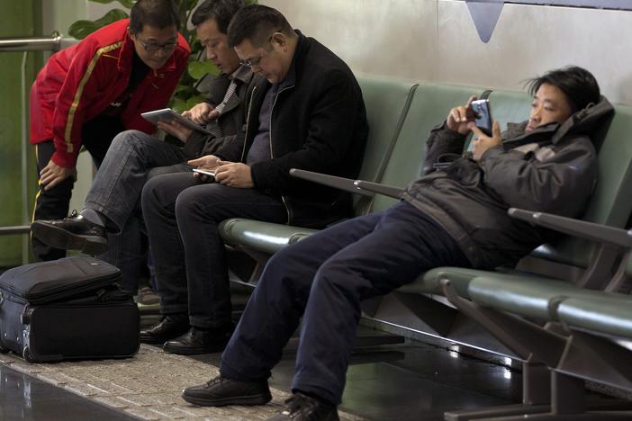 Men browse their tablet computers and smartphone at the Beijing Capital Airport on Nov. 30, 2013.