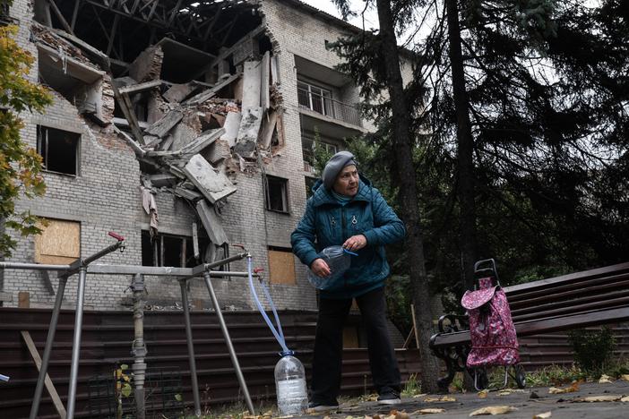 A woman fills bottles with water from a public spigot in front of a bombed out student dormitory in Dobropillya, Ukraine, on Oct. 17.