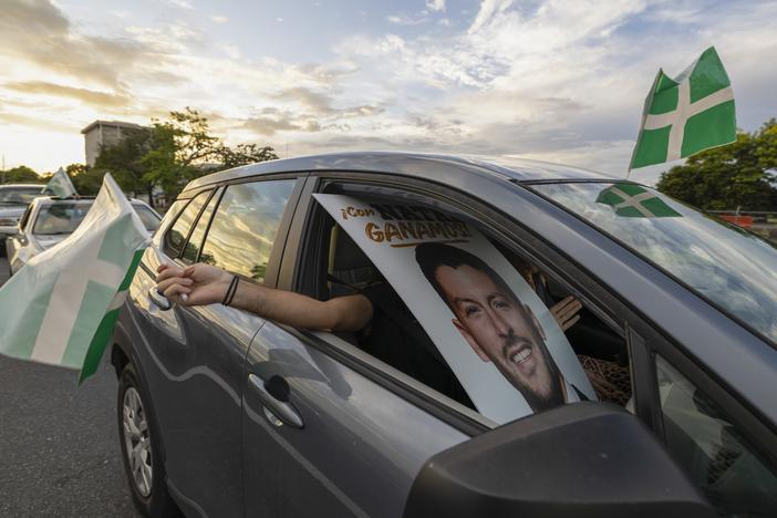 A supporter waves a Puerto Rican Independence Party flag while holding a campaign poster promoting the Citizens' Victory Movement mayoral candidate Manuel Natal, during a caravan in San Juan, Puerto Rico, Friday, Nov. 1, 2024.