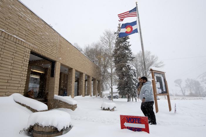 Cristian Ortega carries his son Luca as he walks in the snow into the Oak Creek Town Hall to drop off his ballot on Election Day, November 5, 2024, in Oak Creek, Colorado.