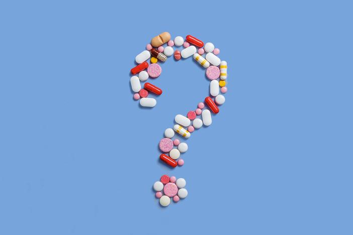 A lot of pills scattered on a blue background. A question mark laid out of pills. Counterfeit medicinal products. Empty space to insert text