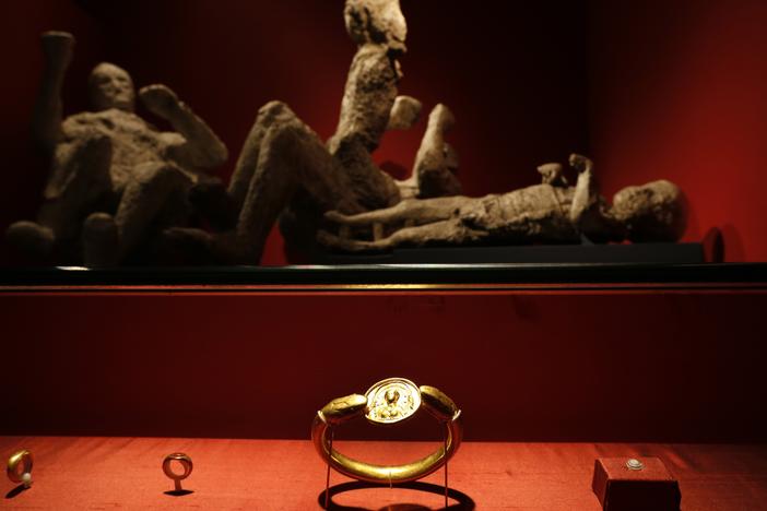 Jewelry found in the ruins of a house in Pompeii are displayed, backdropped by the casts of two adults and two children who died together, are seen housed at the British Museum in London in 2013.