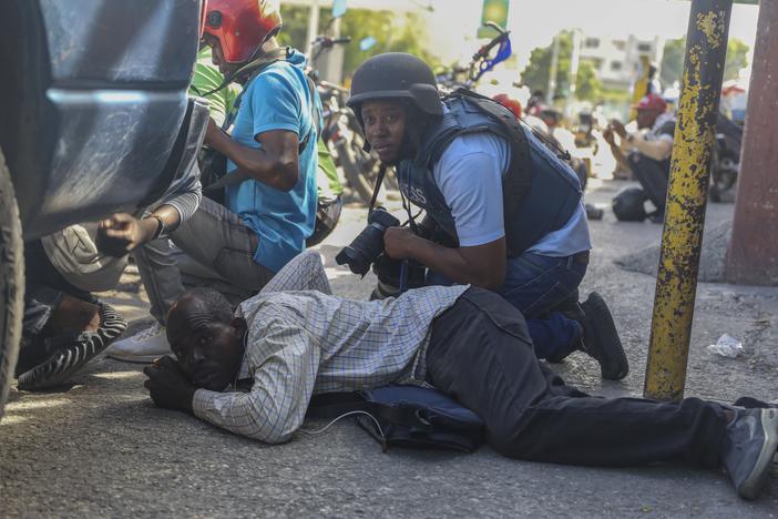 Journalists take cover from the exchange of gunfire between gangs and police in Port-au-Prince, Haiti, Monday.