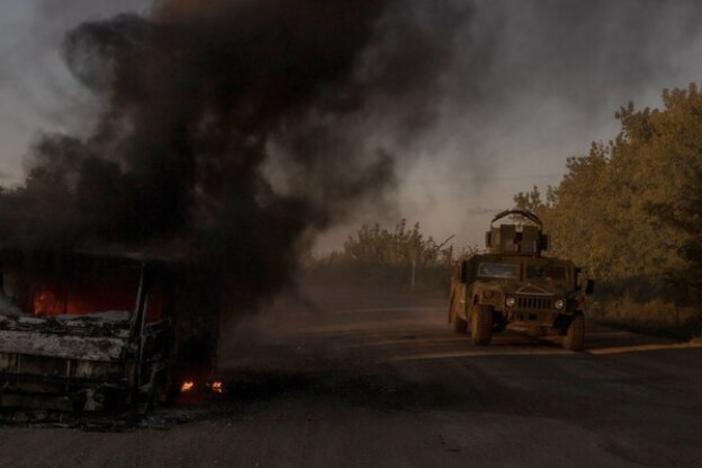 A Ukraine's Humvee armored military vehicle drives past a burning car on a road near the border with Russia, in the Sumy region of Ukraine, on August 14.