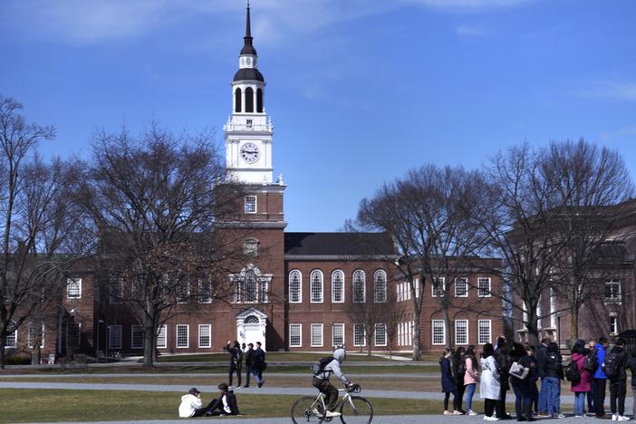 A bicyclist passes a college tour group outside the Baker Library at Dartmouth College, April 7, 2023, in Hanover, N.H.