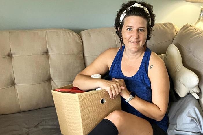 Erica Hayes, 40, sits on her sofa with a box where she keeps the medical supplies she needs to manage her long COVID symptoms, which include chronic fatigue, irregular heart rate, low blood pressure, hives, migraines and internal tremors.