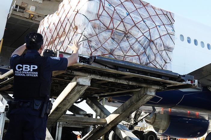 U.S. Customs and Border Protection says it processes some 4 million de minimis shipments every day. Here, CBP officers watch as international shipments are lowered from a plane at Los Angeles International Airport.